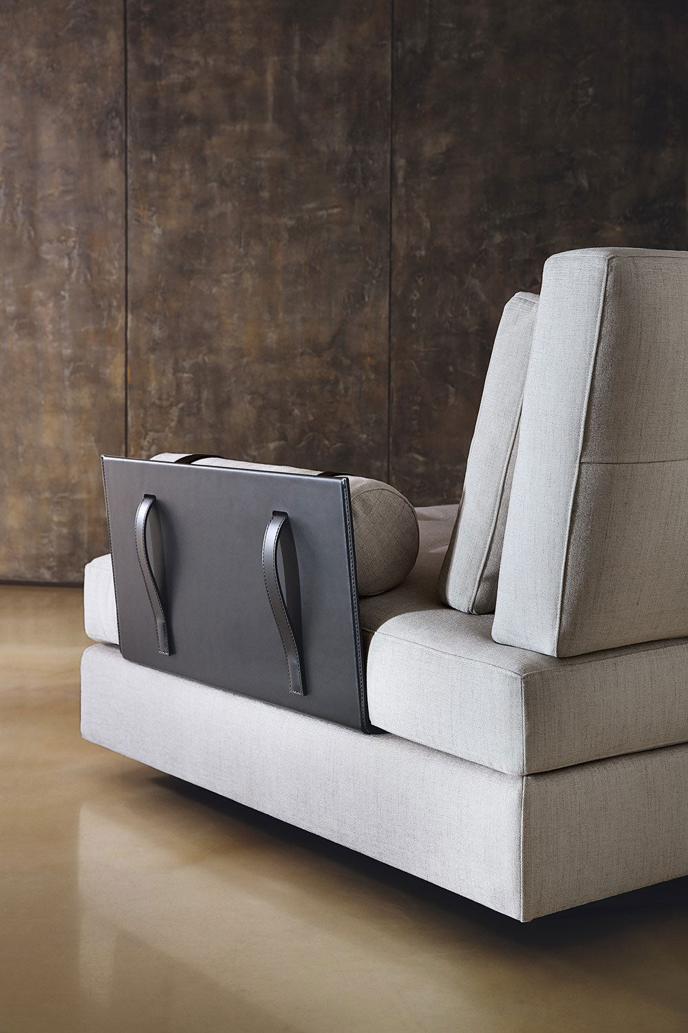 View of light gray fabric sofa with dark leather back panel and handles. 