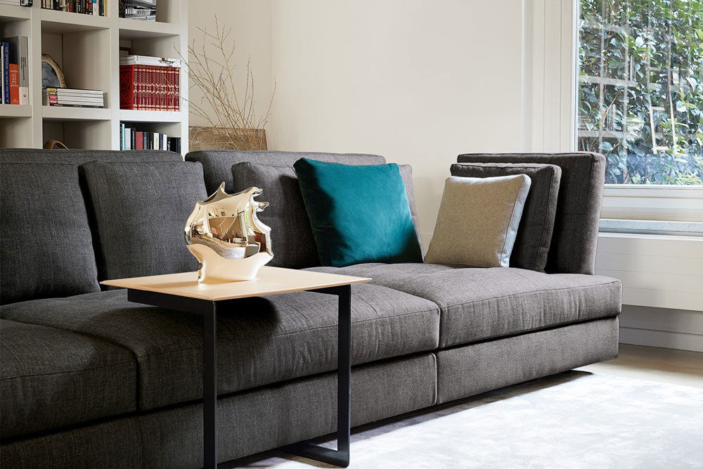 Interior view, dark gray sectional sofa, teal and beige throw pillows, side table, silver boat sculpture, white bookshelf, window, living room furniture.