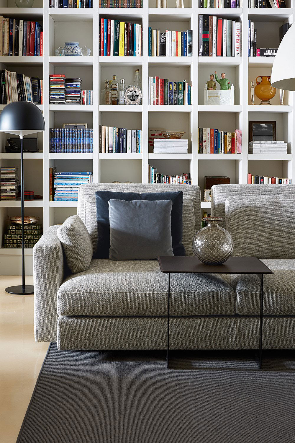 Living room with gray sofa, dark side table, floor lamp, white bookshelf, gray rug