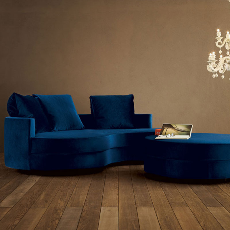 Curved blue velvet sofa with ottoman on wood floor