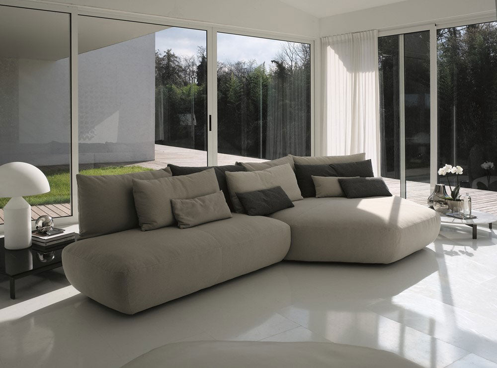 Modern sectional sofa with pillows in sunlit living room overlooking garden