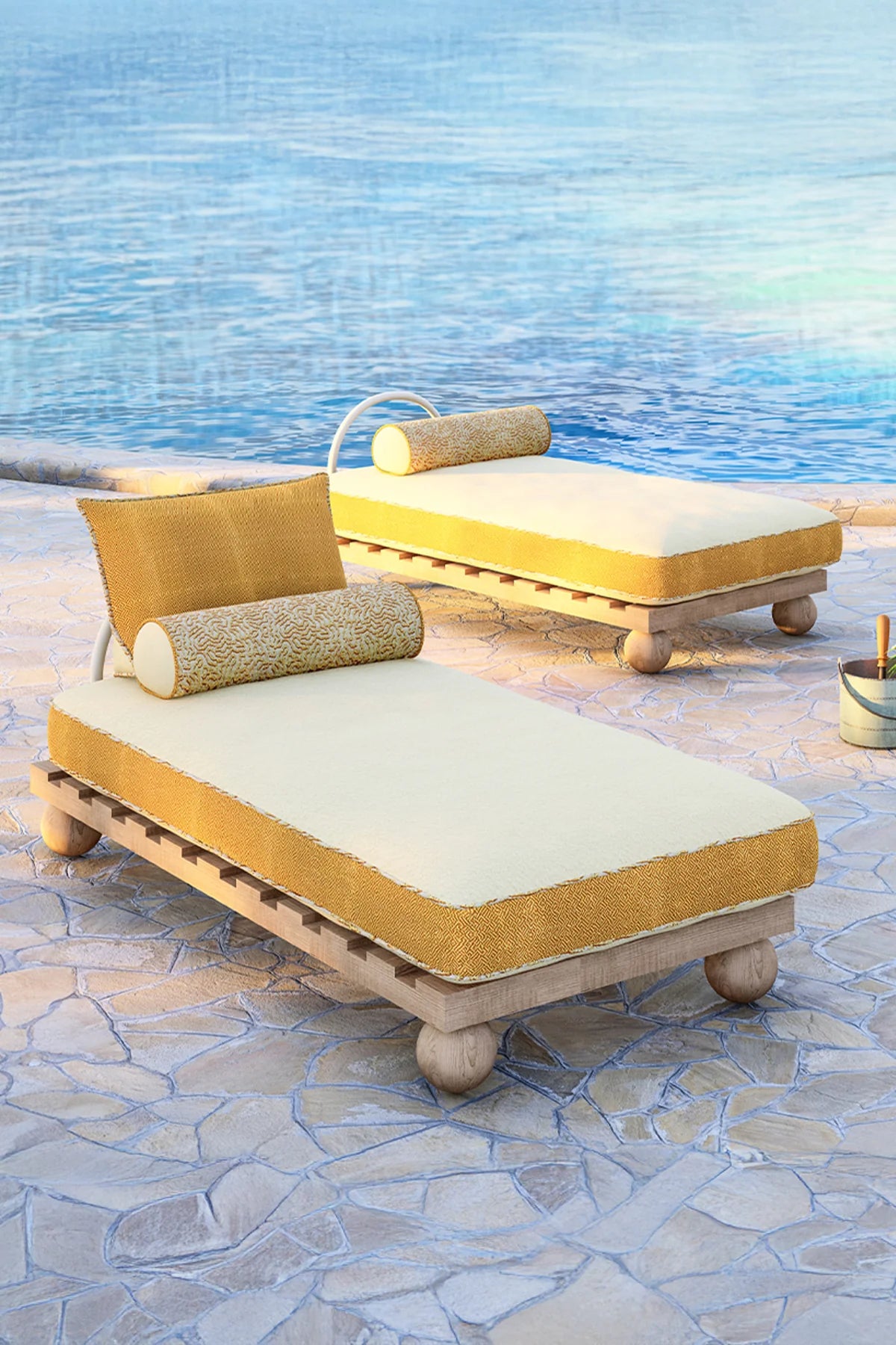Two yellow outdoor lounge chairs with cushions on a stone patio by a pool.
