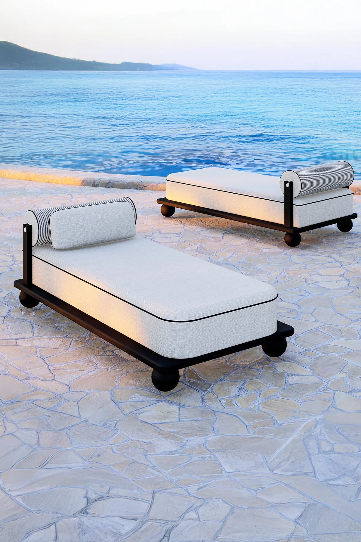 Luxury outdoor sunbed in black finish with cylindrical back pillow on stone terrace.