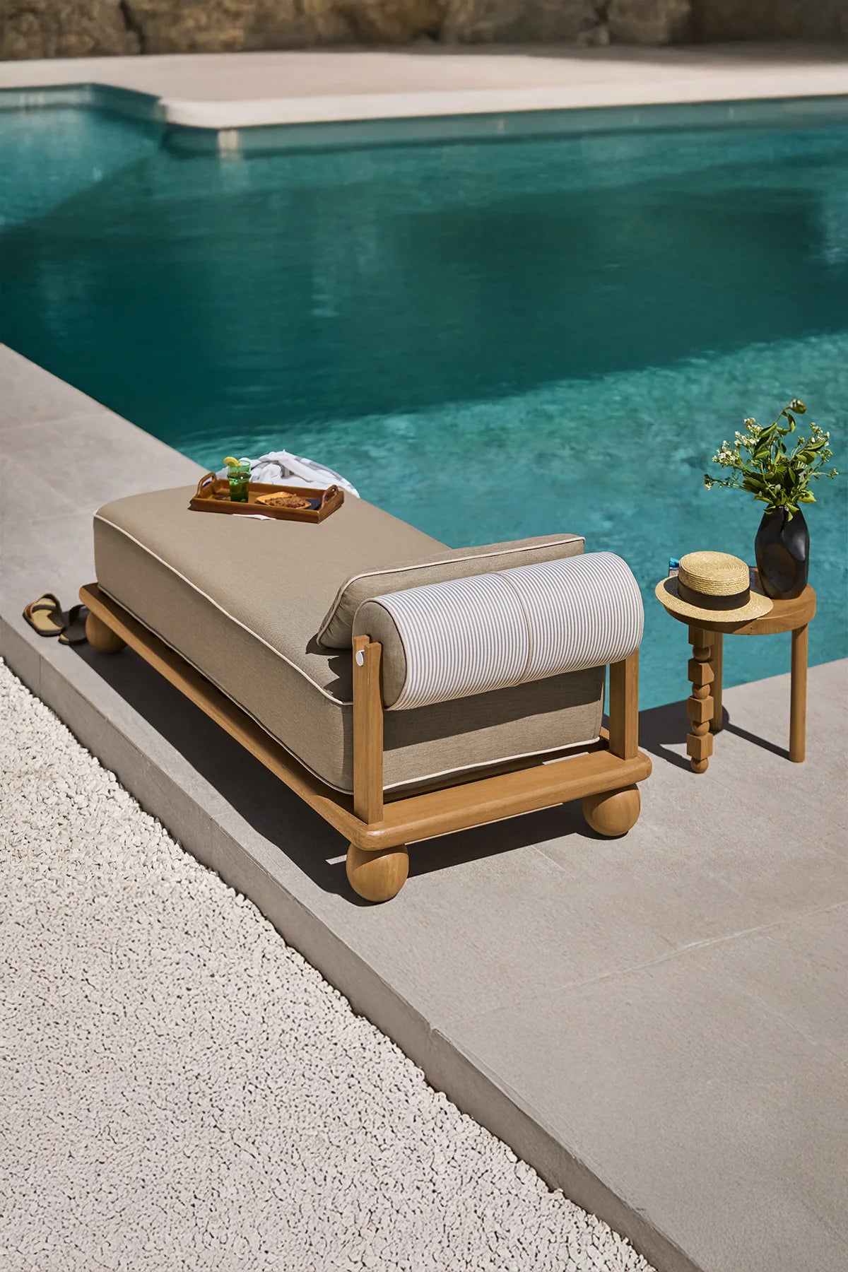 Beige outdoor lounge chair by a pool with a small table and plants.