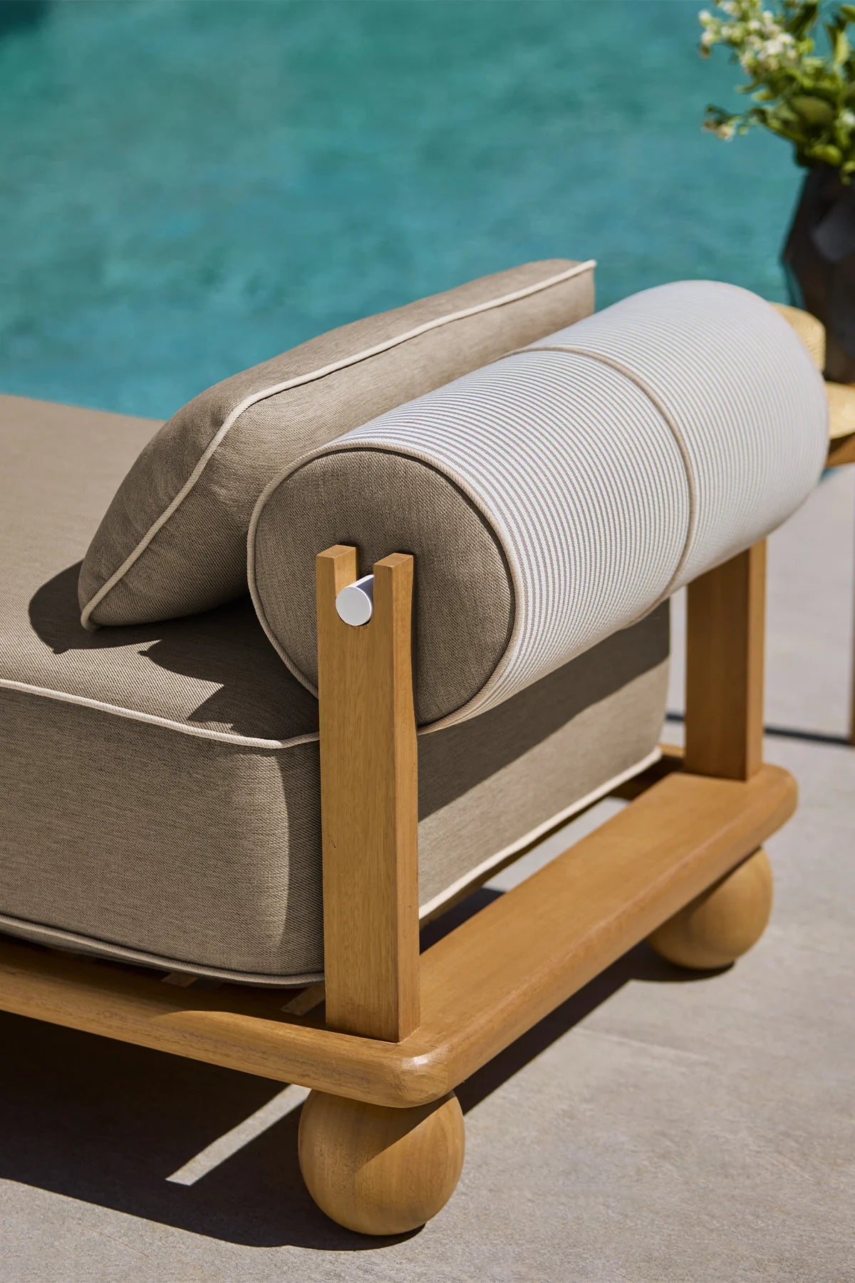 Beige outdoor lounge chair with wooden frame and cushions by a pool.