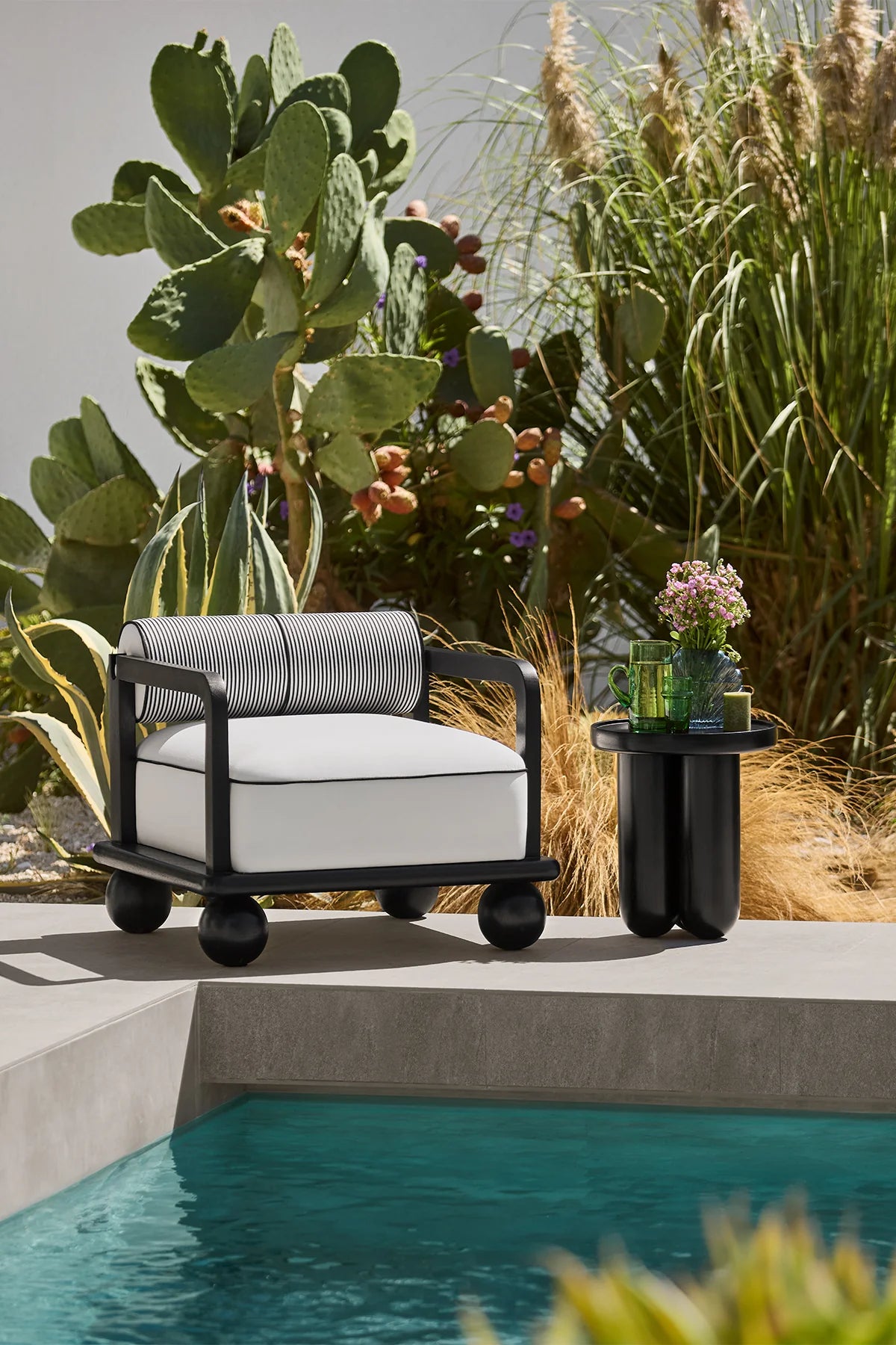 Modern outdoor chair with white cushion by a poolside with cacti and plants.
