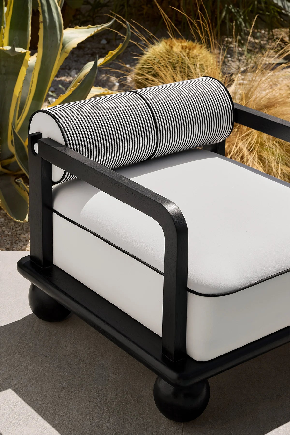Modern outdoor lounge set with iroko wood frame, white cushions, and black accents on a garden terrace.