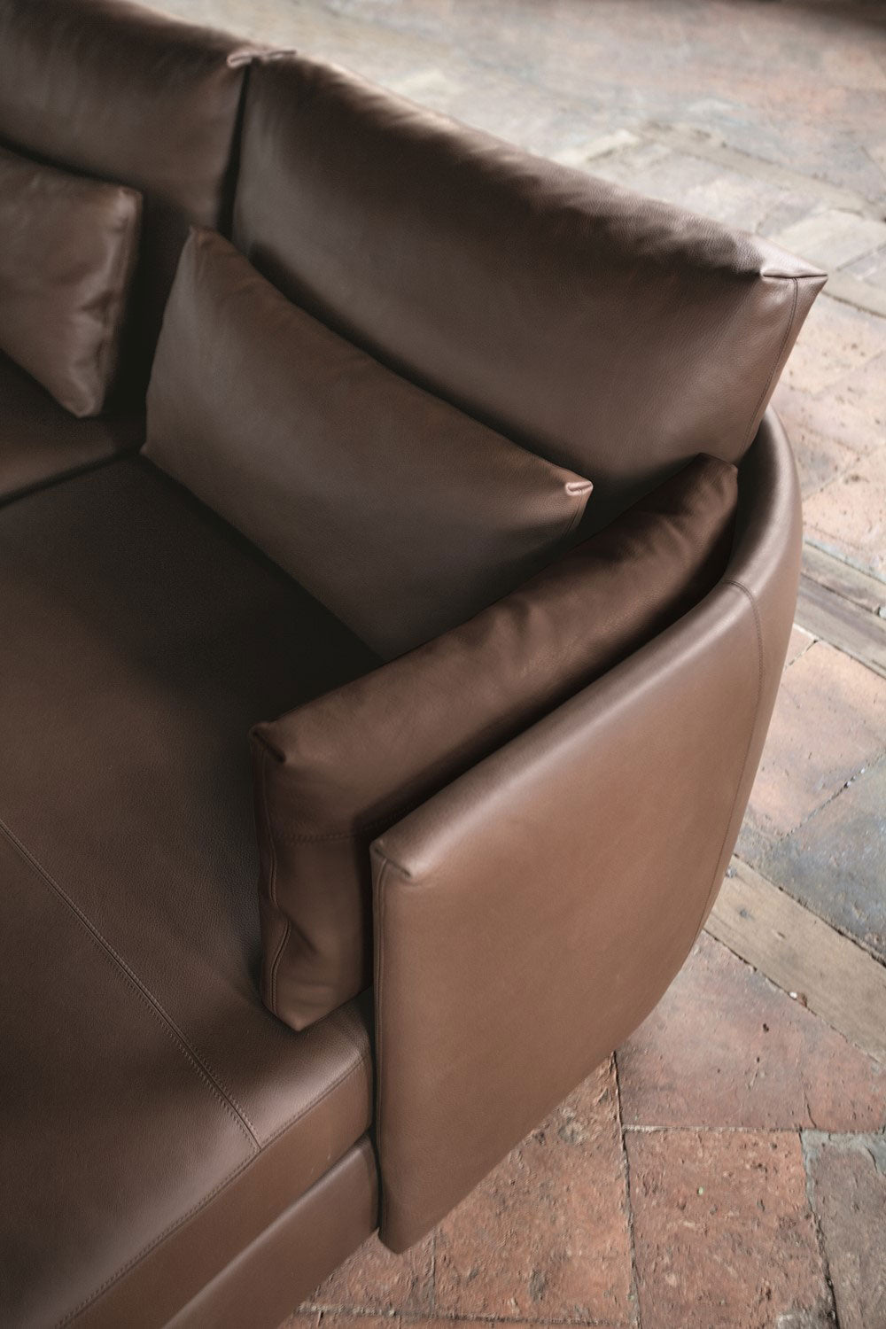 Close up brown leather sofa cushions and armrest on brick floor