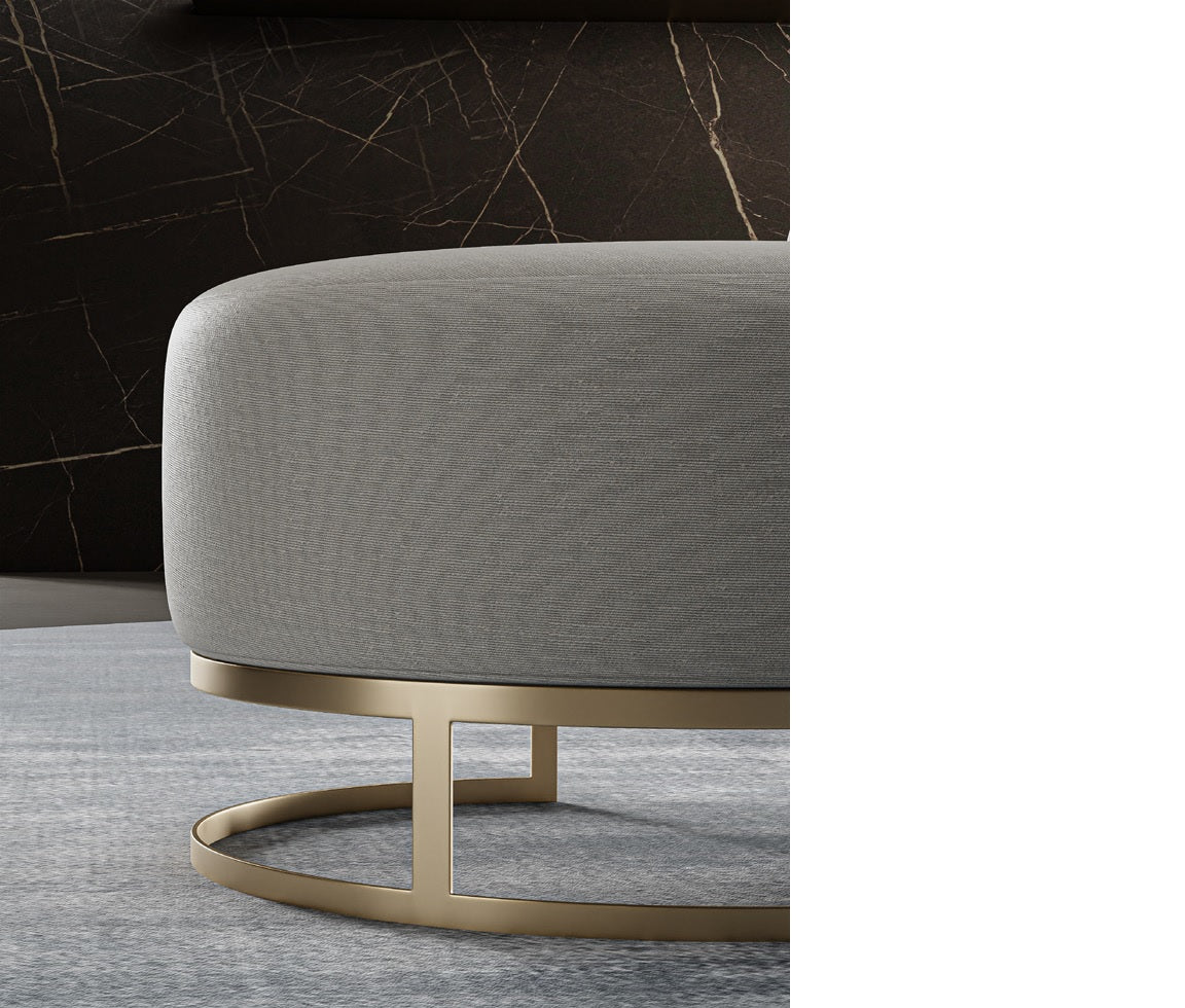 Close up view of gray fabric ottoman with gold metal base on rug.