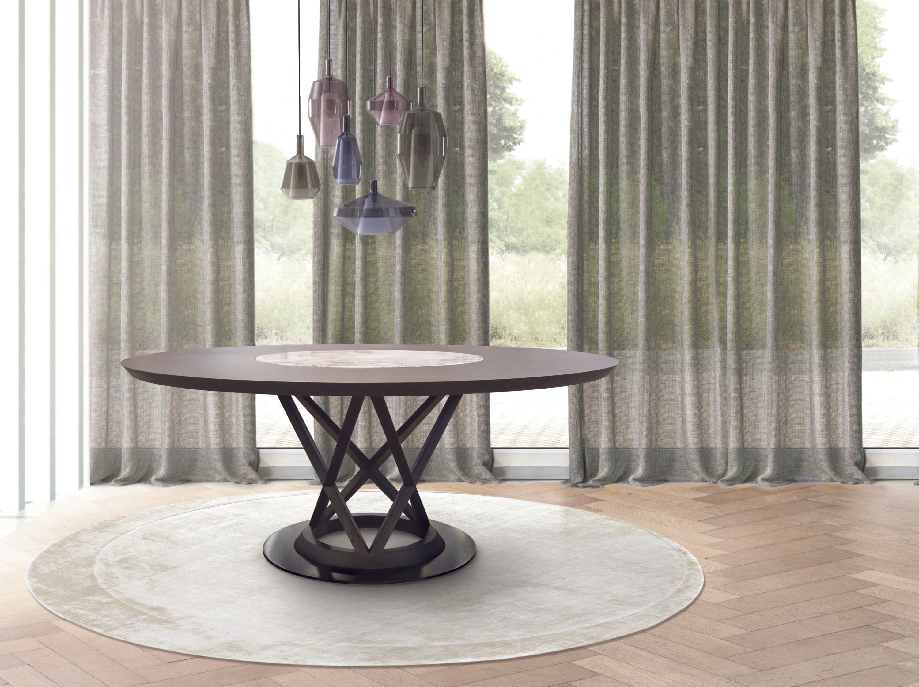 View of dining room with round wood table, glass pendant lighting, sheer curtains, round rug, wood floor.