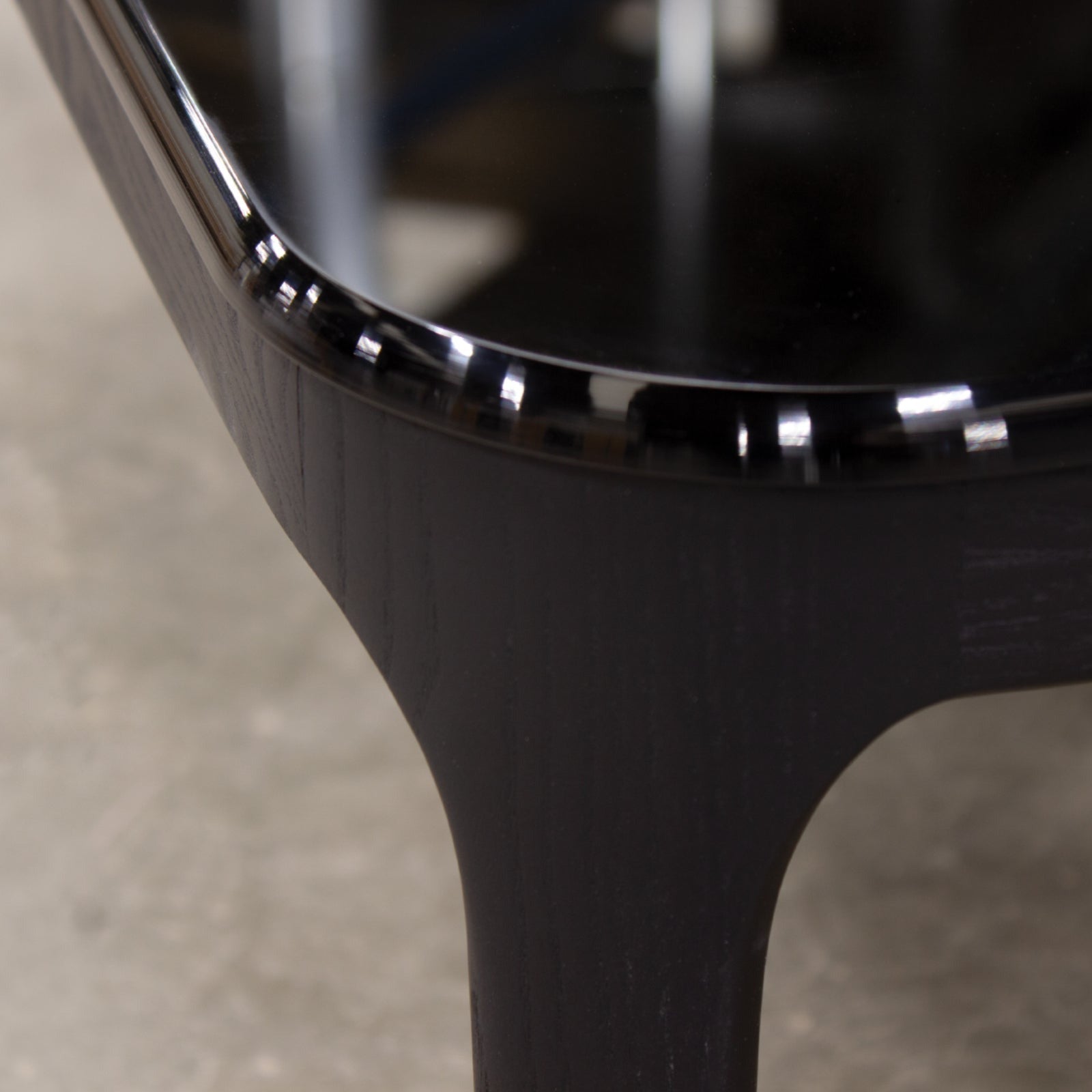 Close up of black wood table edge and leg on concrete floor.