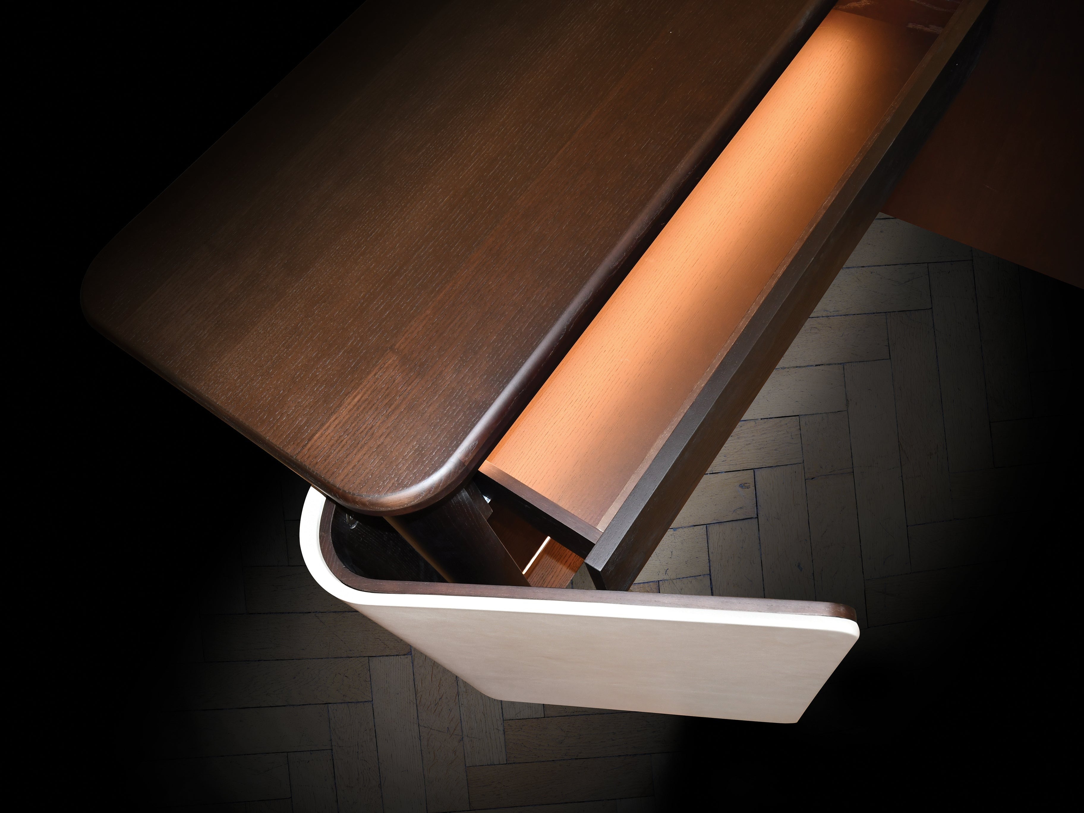 Overhead view of dark wood desk with open drawer and light wood paneling