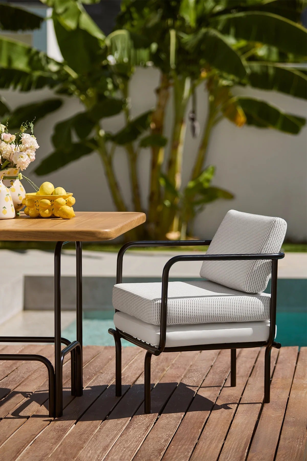 Outdoor setting with a chair and table near a pool, surrounded by plants.