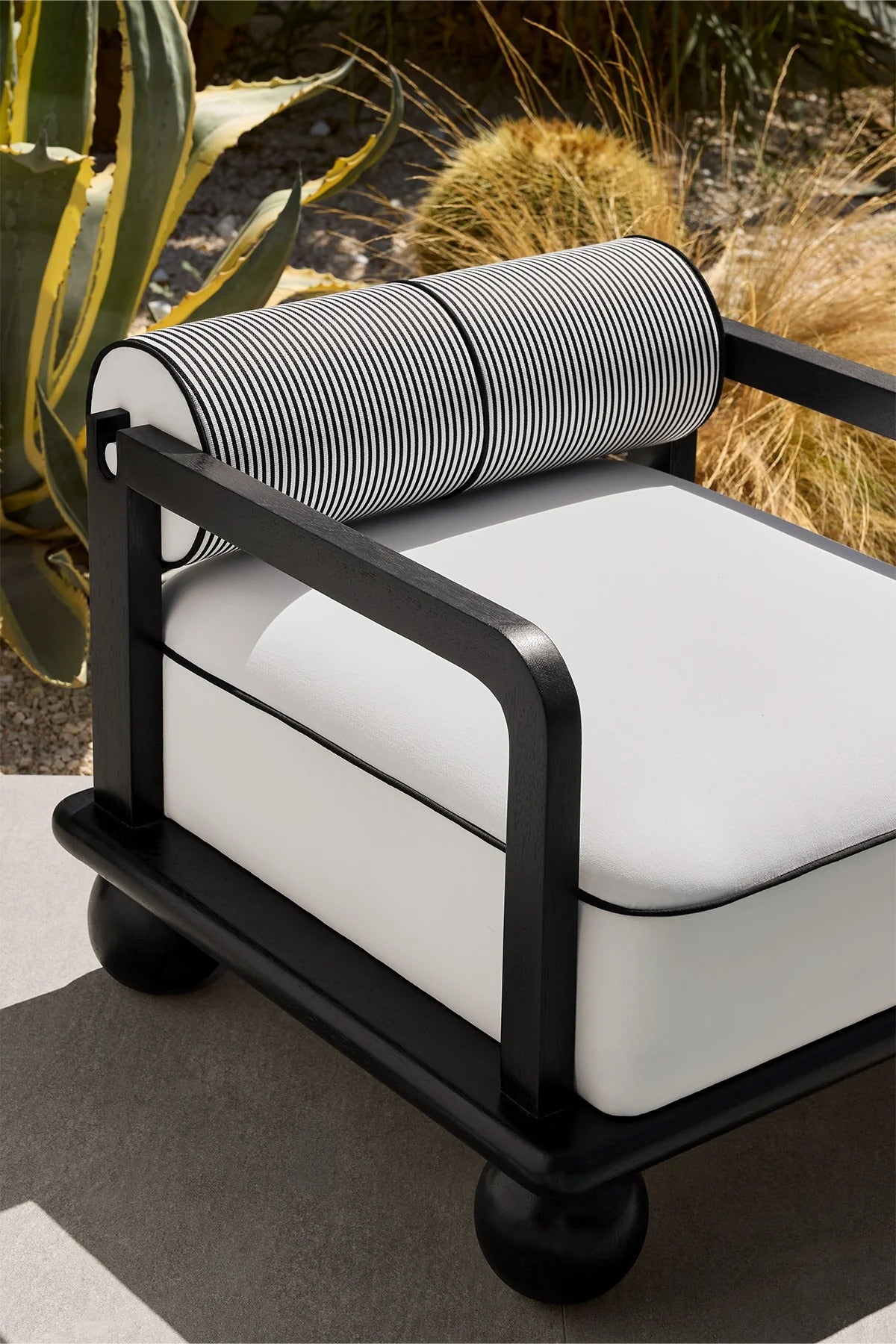 A modern outdoor armchair features a black wood frame and a white cushion, set among plants.