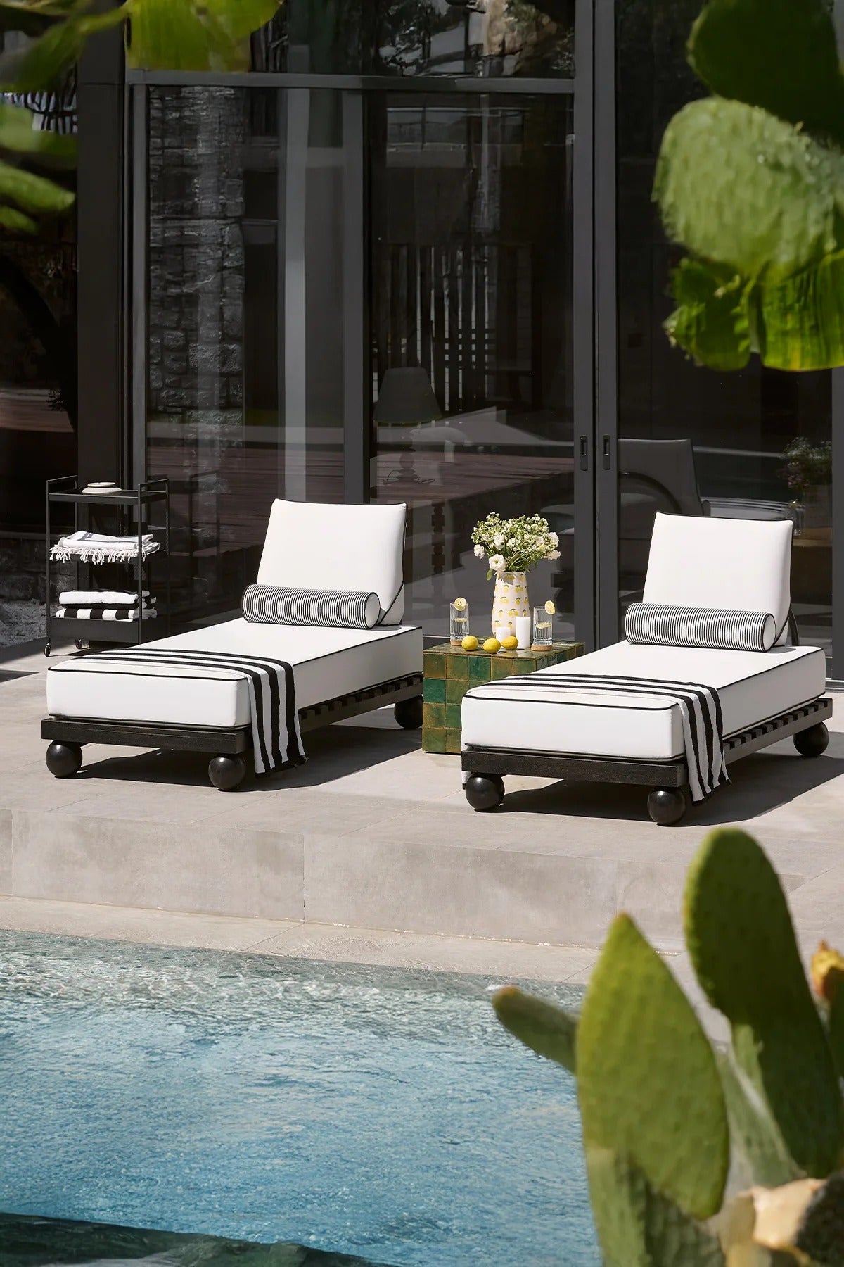 Two lounge chairs with striped covers by a poolside.