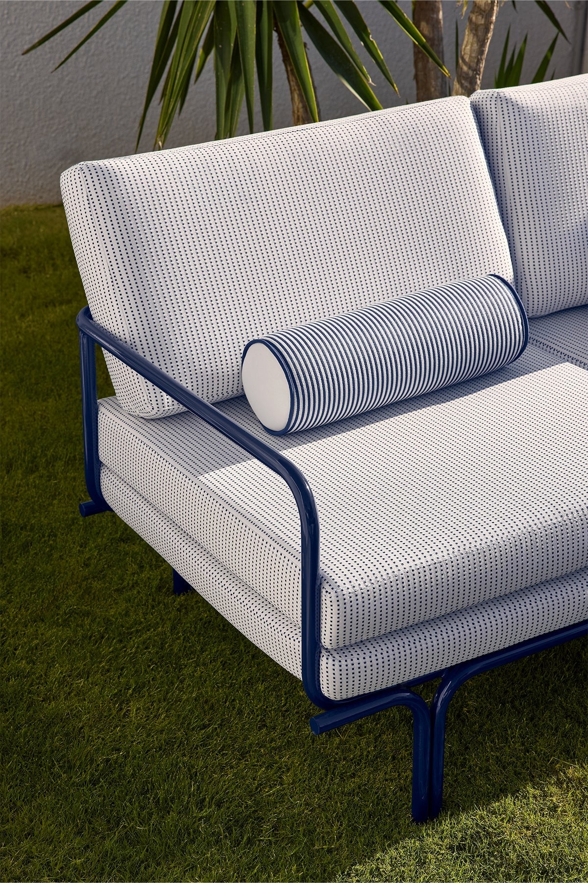 Outdoor sofa with patterned cushions and striped bolster pillow on grass.