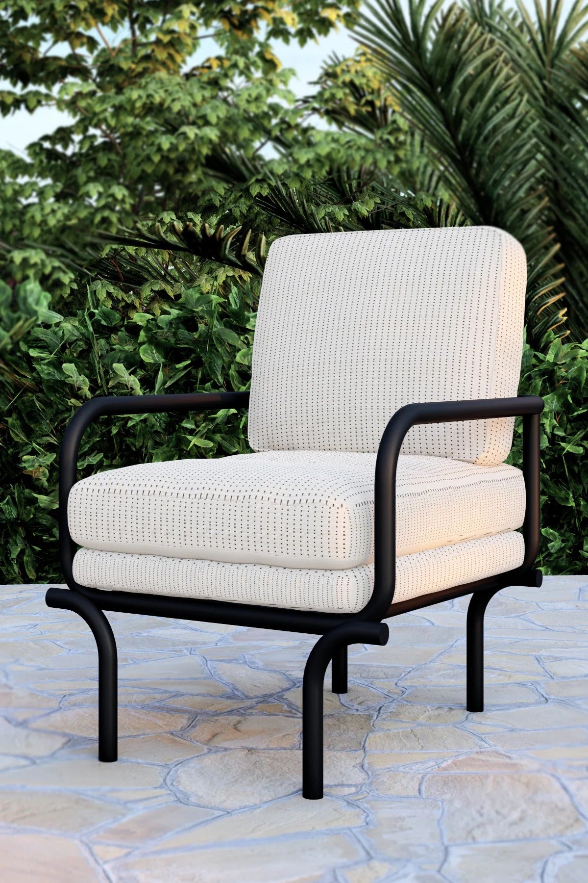 White cushioned chair with black metal frame on a stone patio with greenery in the background