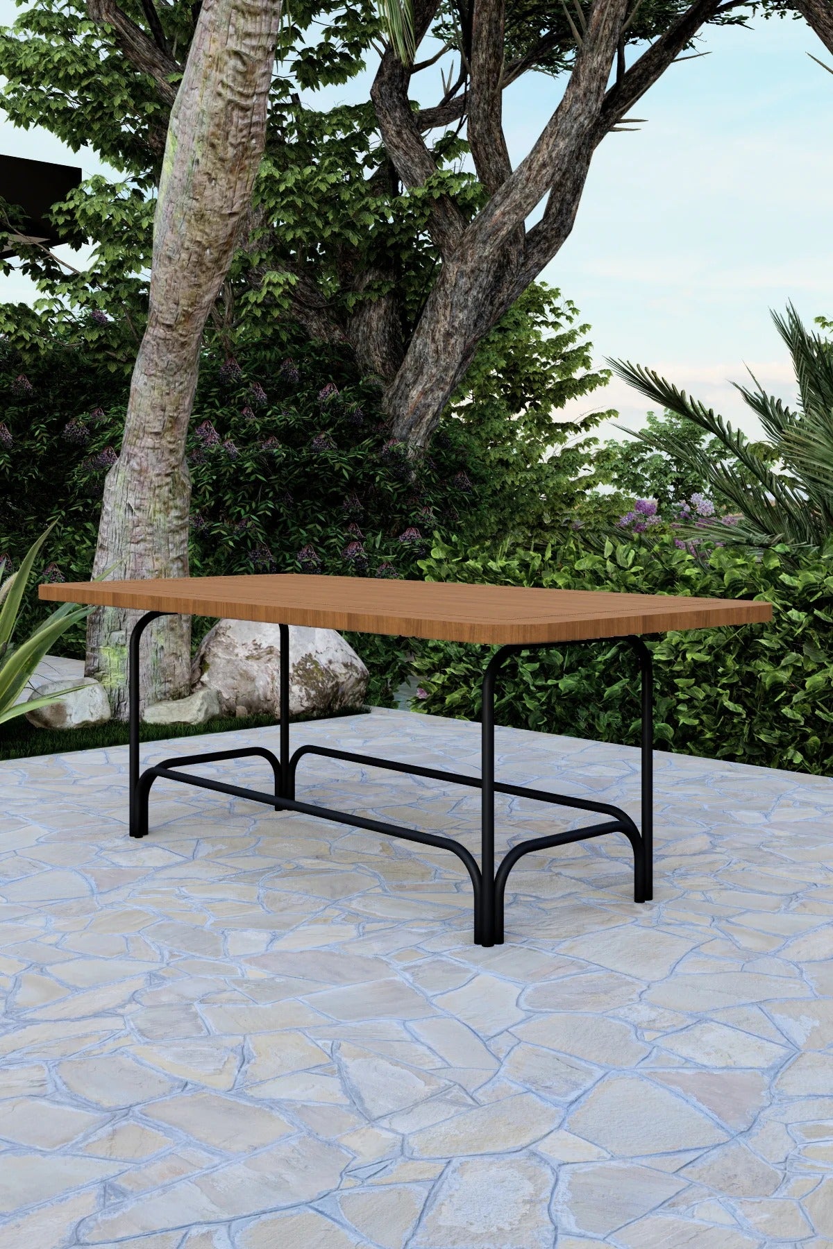 Wooden table with black metal legs on a stone patio with greenery in the background