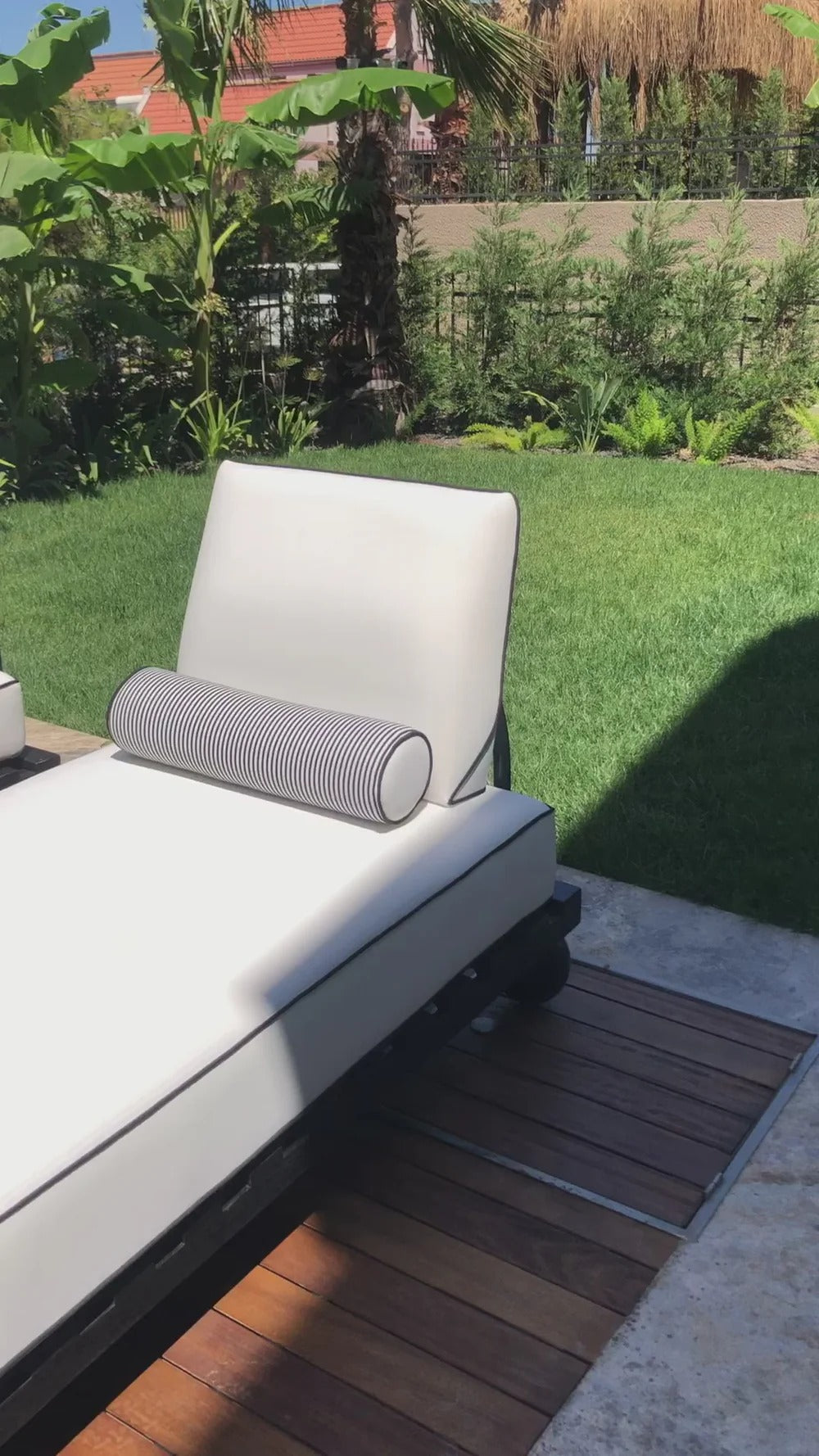 White outdoor lounge chair with gray pillow on a wooden deck with greenery in the background