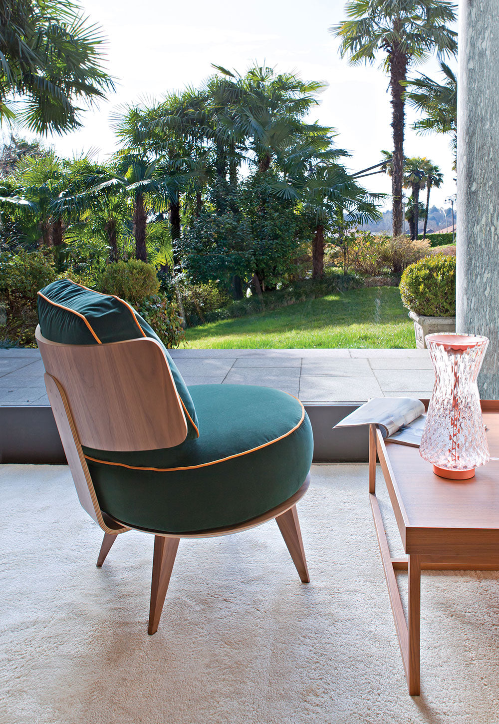 Green velvet armchair and wood table overlooking tropical garden.