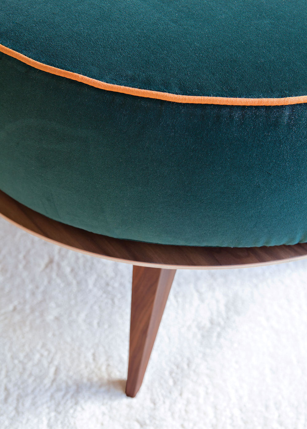 Close-up of green velvet ottoman with orange piping and wood legs
